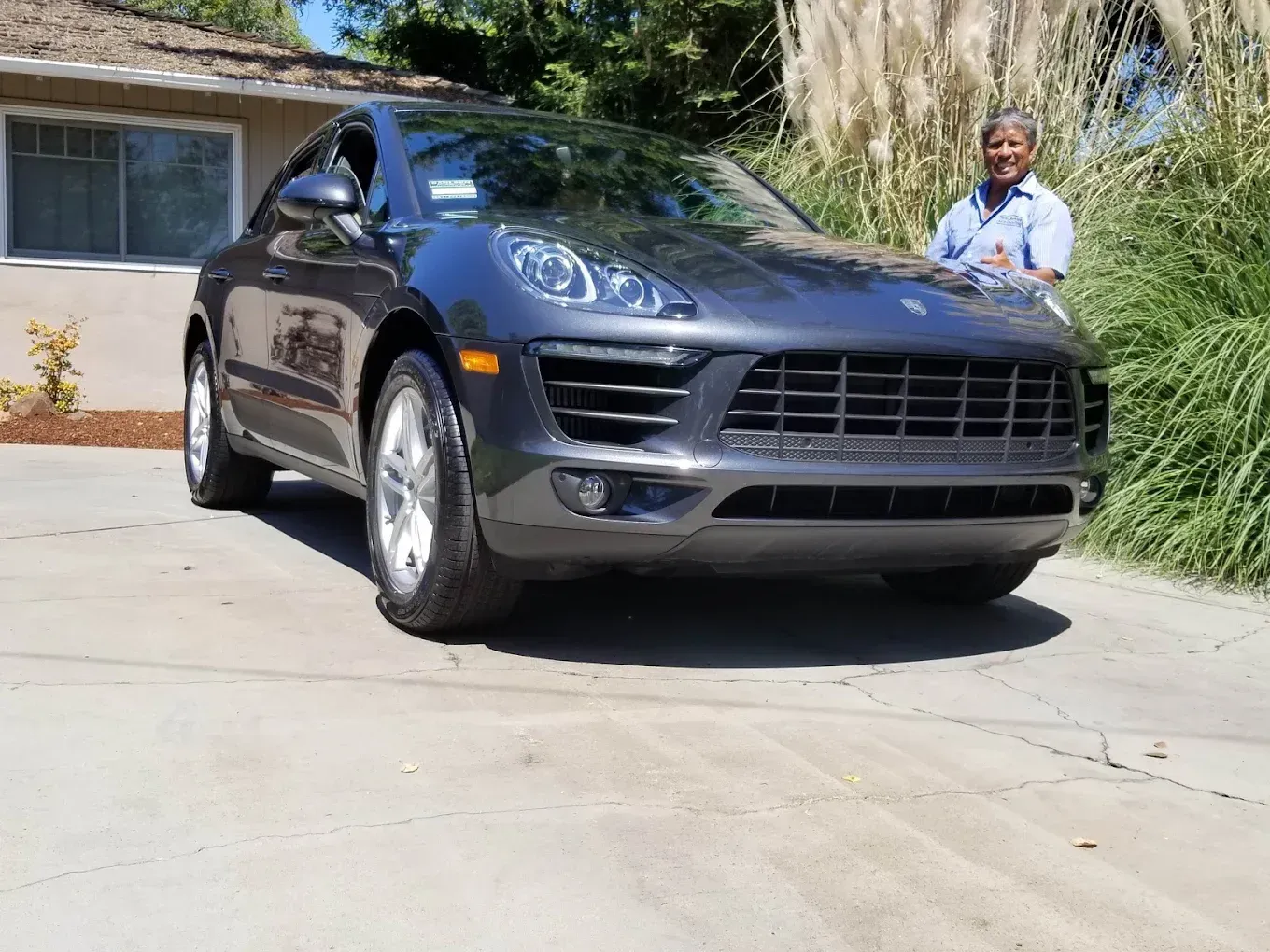Gray Porsche SUV with a person smiling, parked in a driveway.