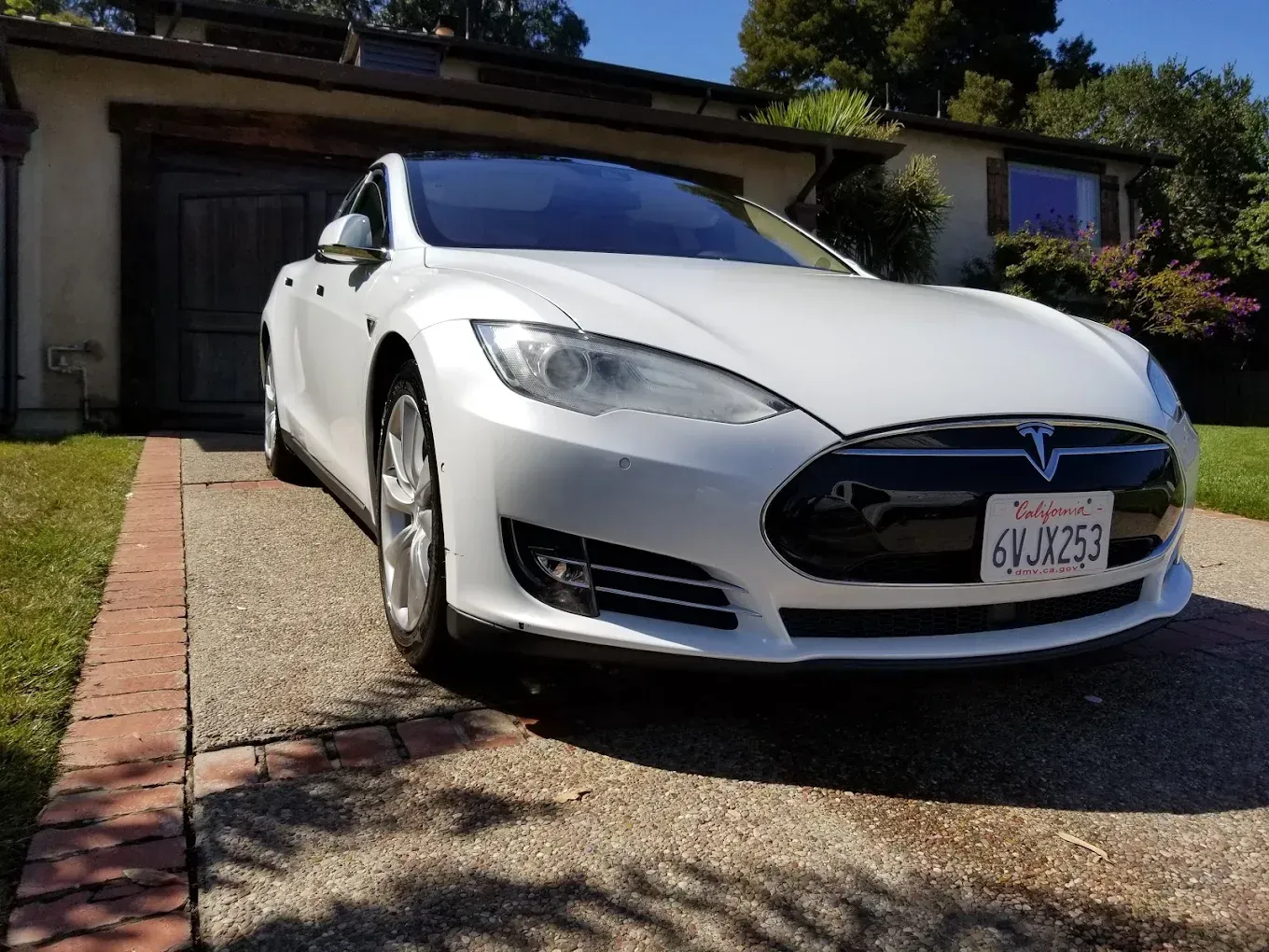 White Tesla Model S parked in a driveway in front of a house.