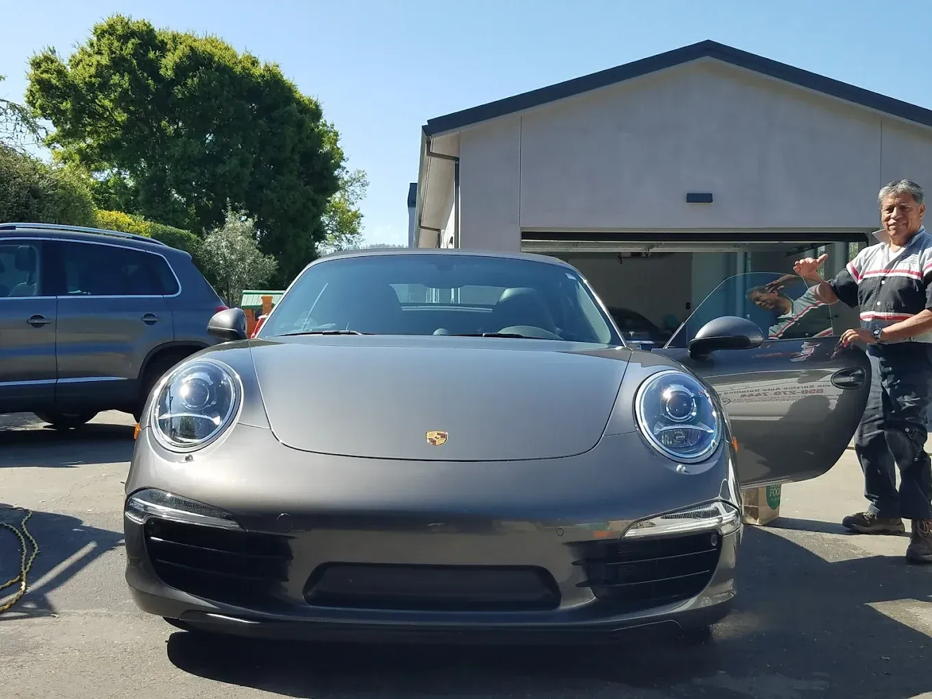 Gray Porsche car with open door, man next to it, parked in front of a building.