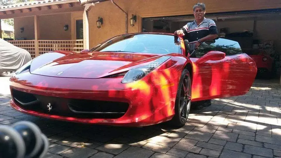 Man standing next to a red Ferrari with the door open. Garage in the background.