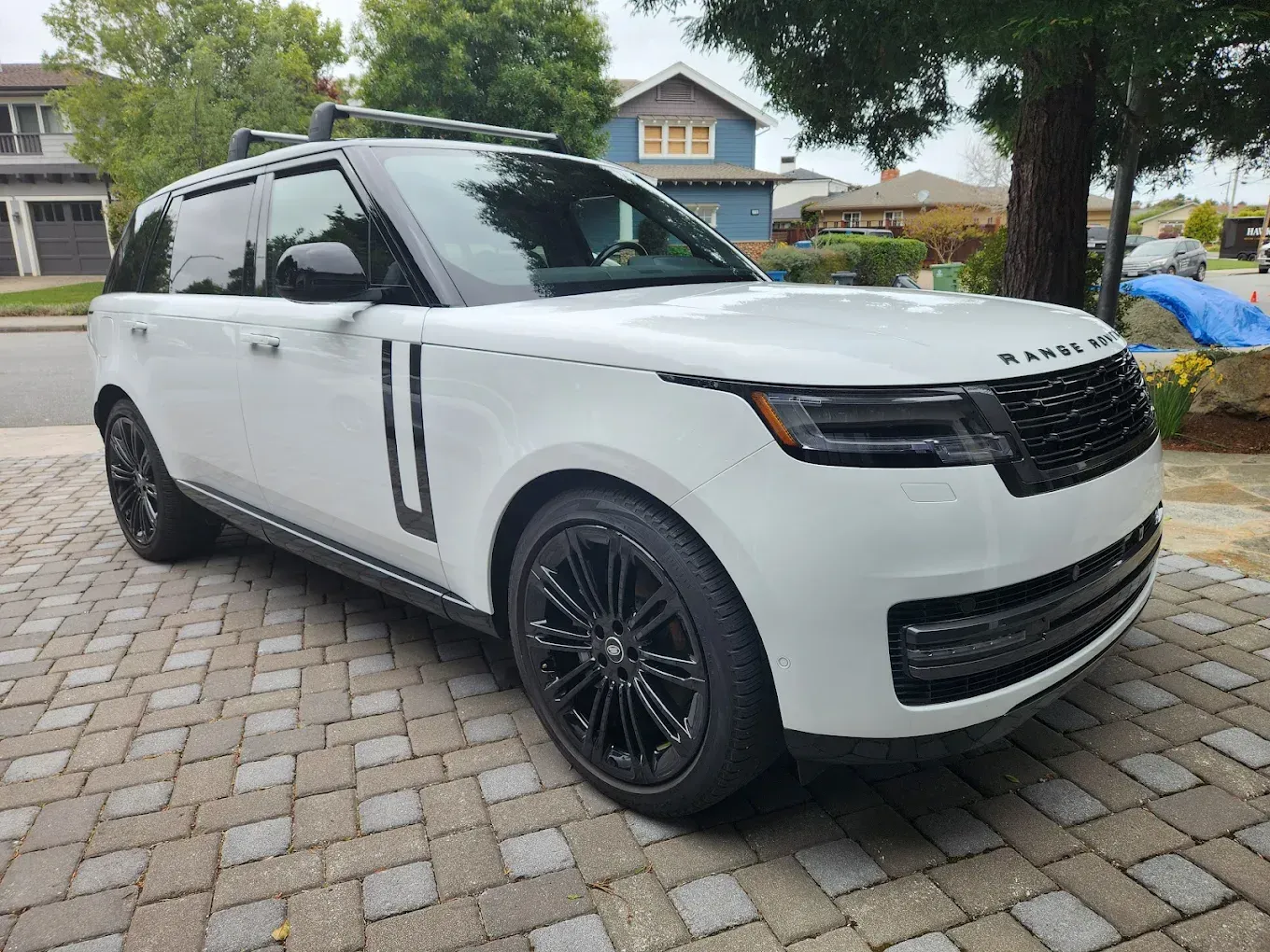 White Range Rover SUV parked on a brick driveway, black wheels and roof rack.