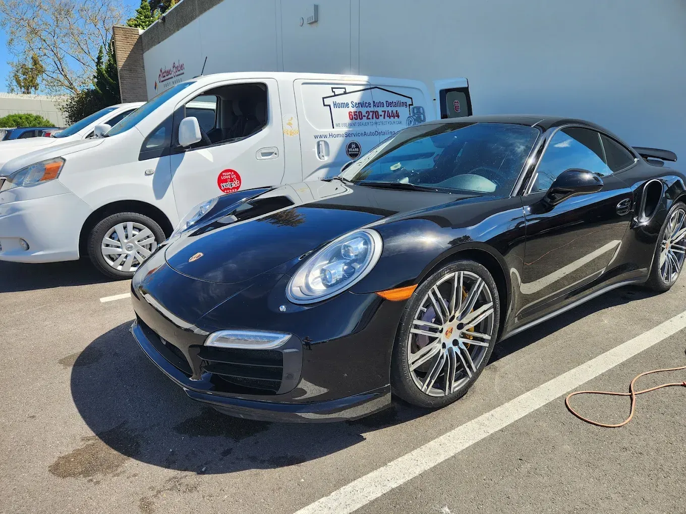 Black Porsche parked next to a white van with business logo on a sunny day.