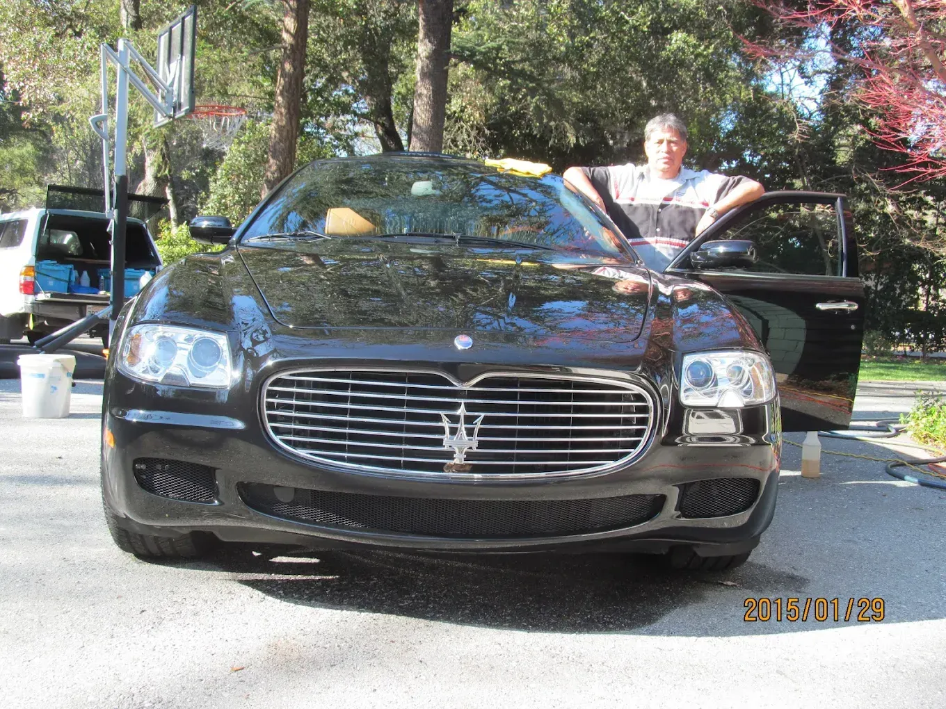 Man leaning on a black Maserati parked in a driveway.