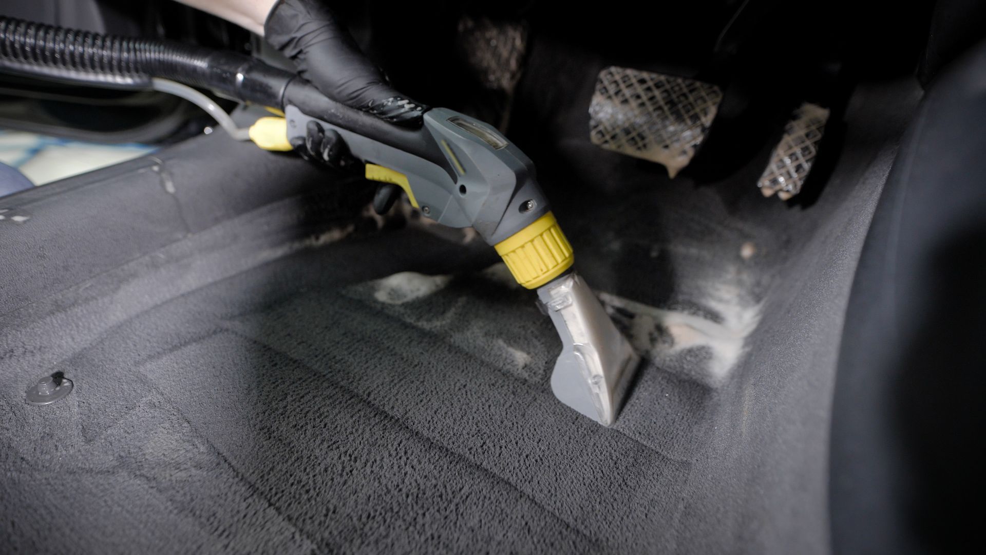 A person using a cleaning tool to clean a car's gray carpeted floor.