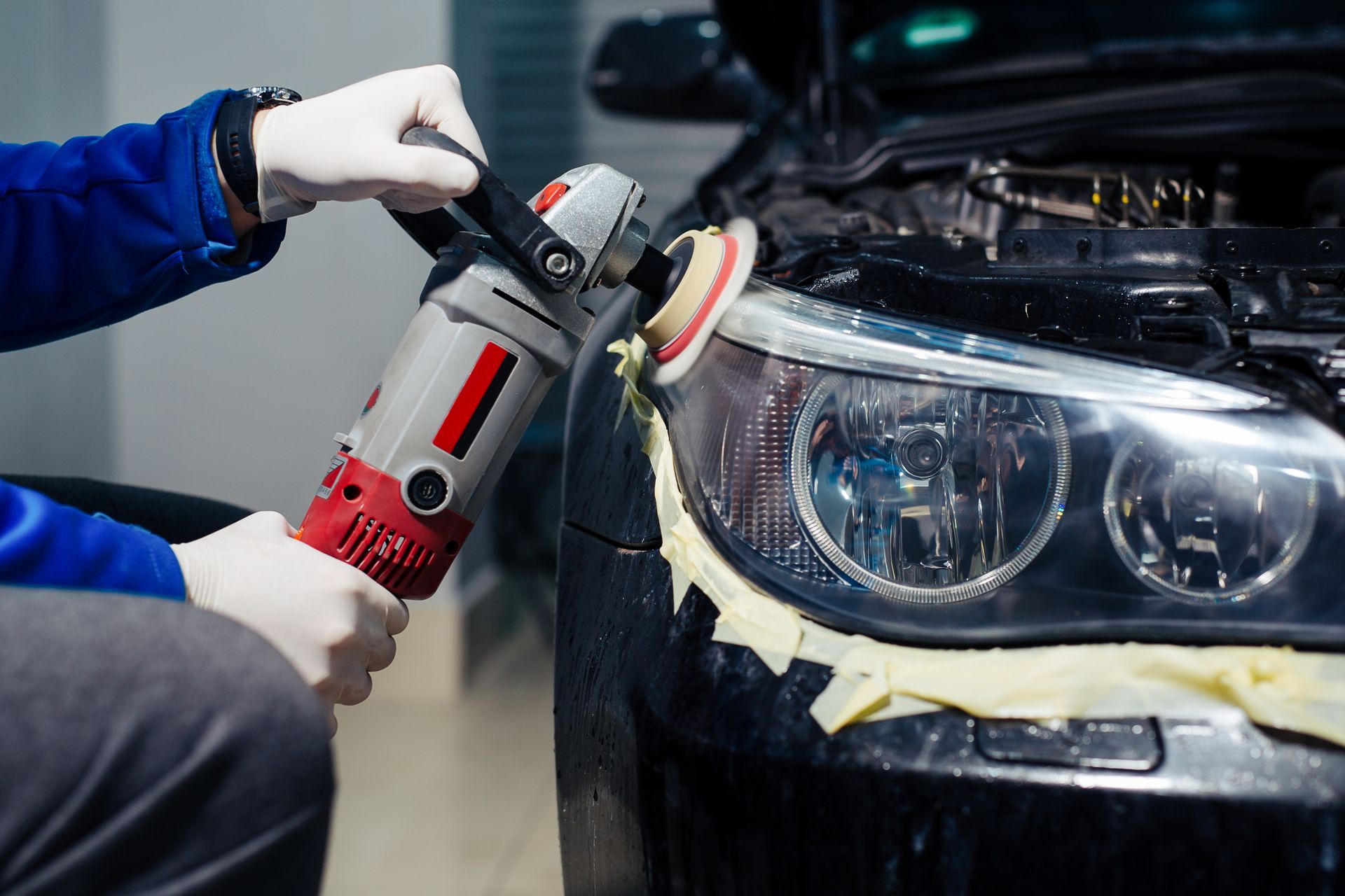 Person in gloves polishing a car headlight with a power tool.