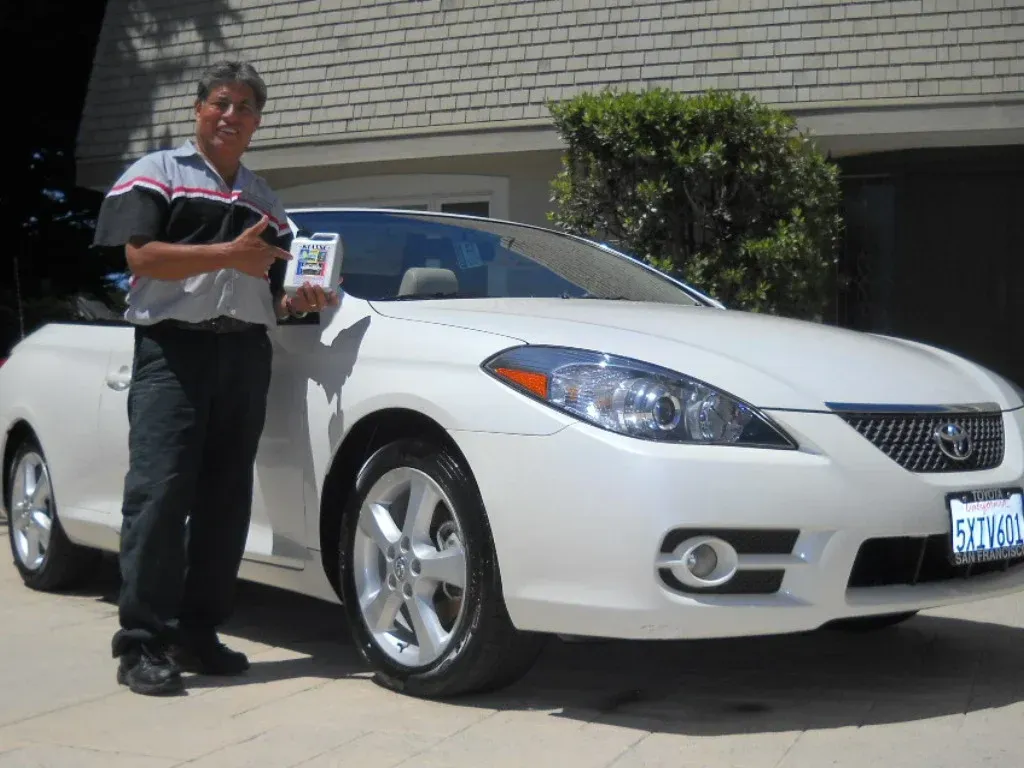 Man in mechanic uniform stands next to a white convertible car.