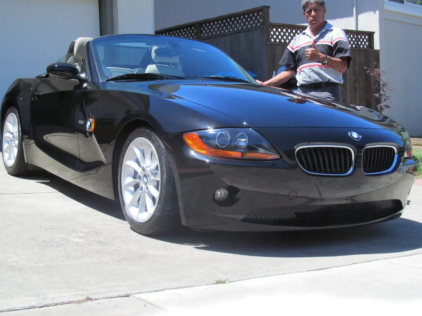Black BMW Z4 convertible parked on driveway; man stands next to car.