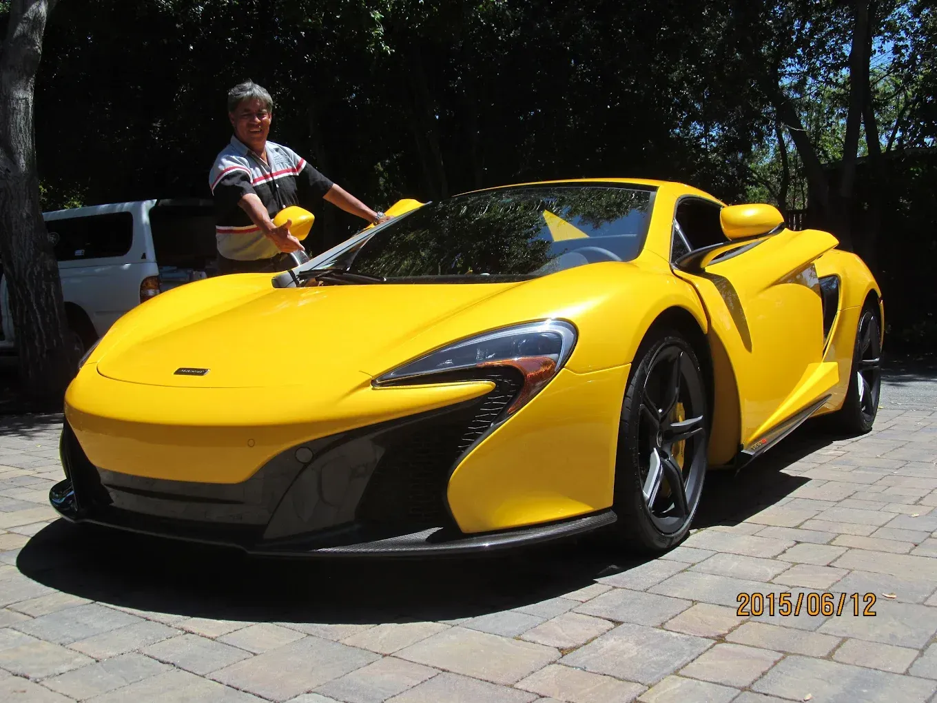 Yellow McLaren sports car with person in polo shirt on sunny day.