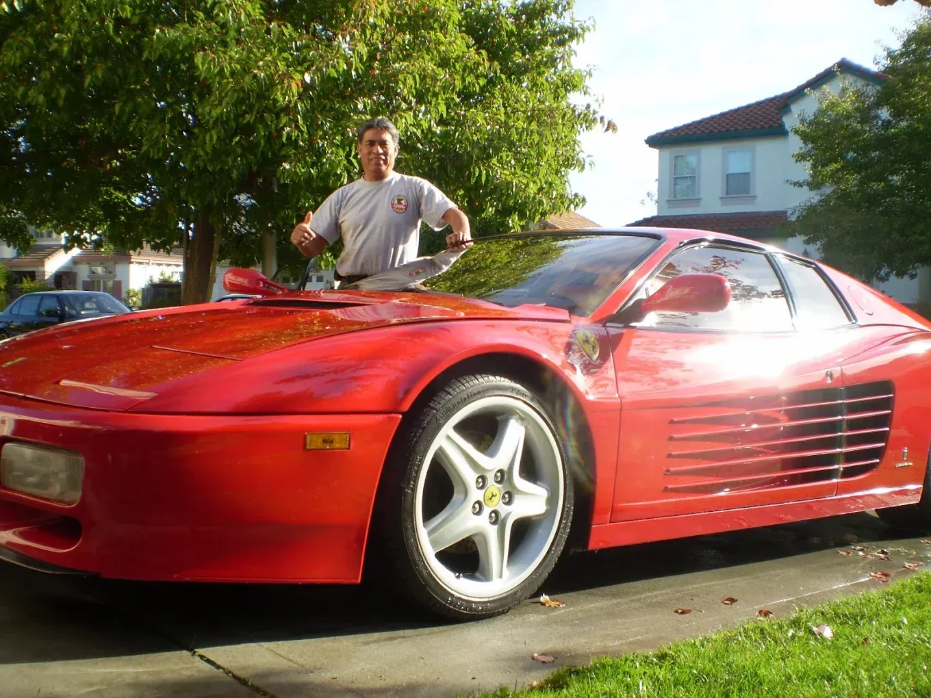 Man washing a red Ferrari sports car in a driveway on a sunny day.