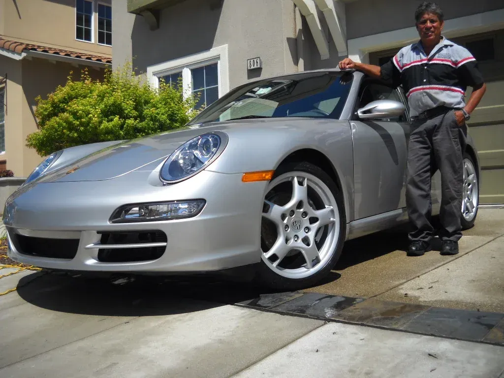 Man standing next to a silver Porsche car in front of a house.