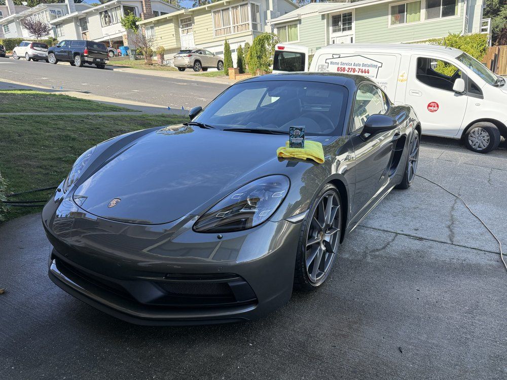 Gray Porsche sports car parked on a driveway with a detailing van in the background.