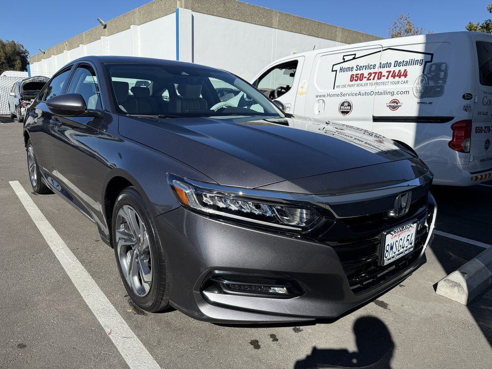 Gray Honda Accord parked in a lot, with a white van in the background. Sunny day.