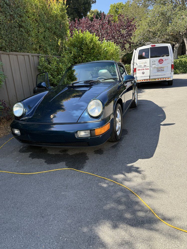 Dark blue Porsche parked on asphalt next to a van; sunny day.