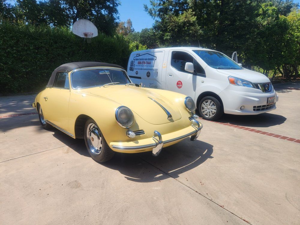 Yellow vintage Porsche convertible and white van parked on pavement.