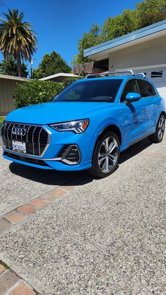 Blue Audi Q3 parked on a concrete driveway in front of a house on a sunny day.