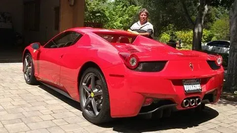 Red Ferrari parked on cobblestones with a man in background.