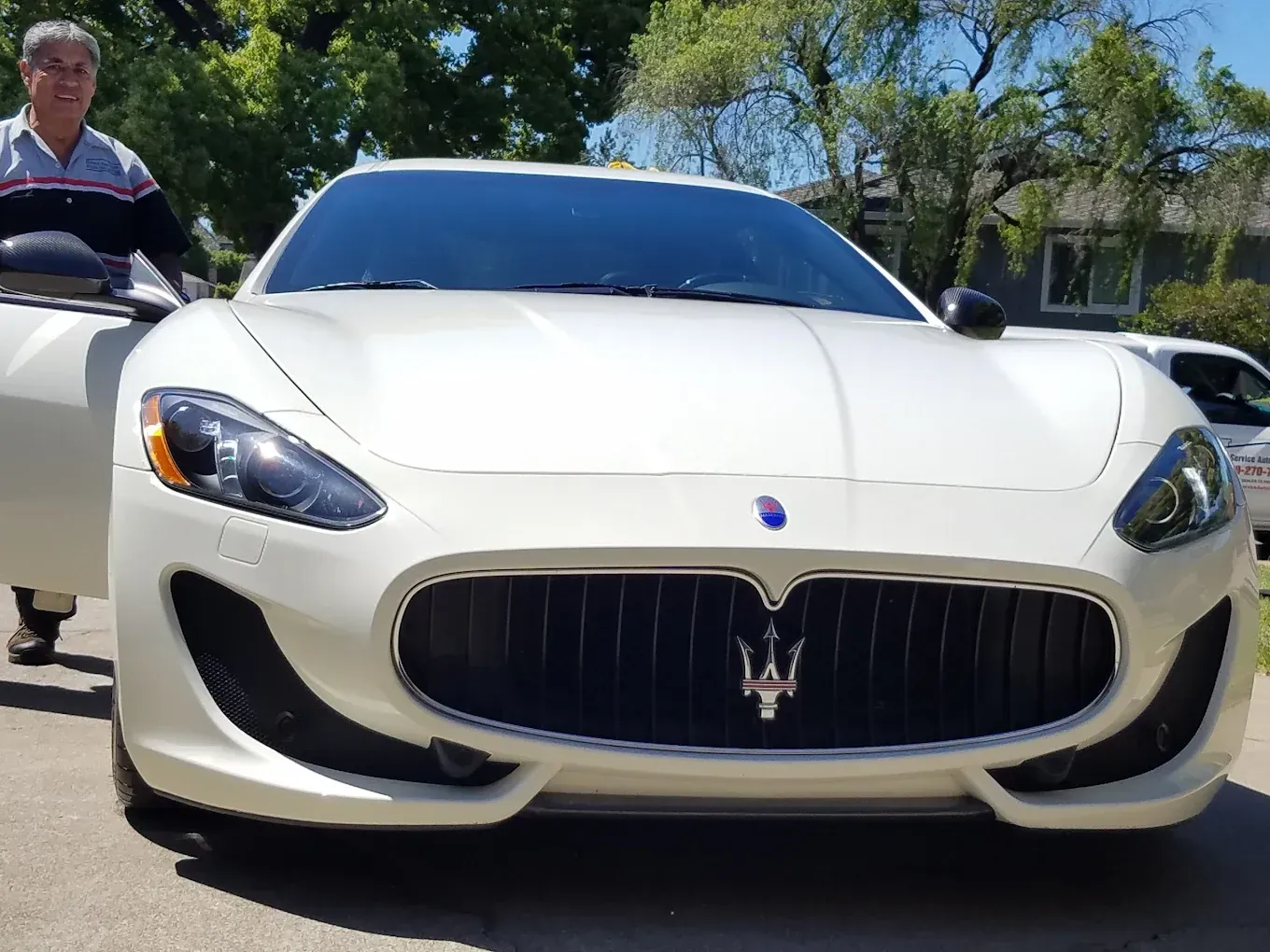 White Maserati car with open door, man standing beside it.