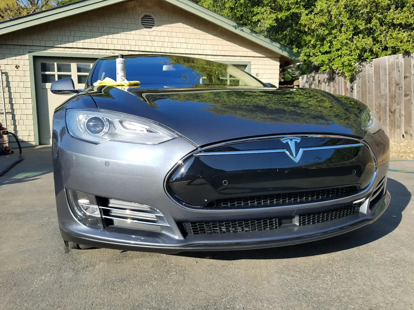 Gray Tesla Model S parked in front of a garage, with a yellow cloth on the windshield.