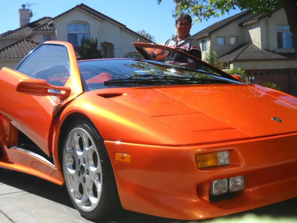 Orange Lamborghini with a man cleaning the windshield in front of a house.