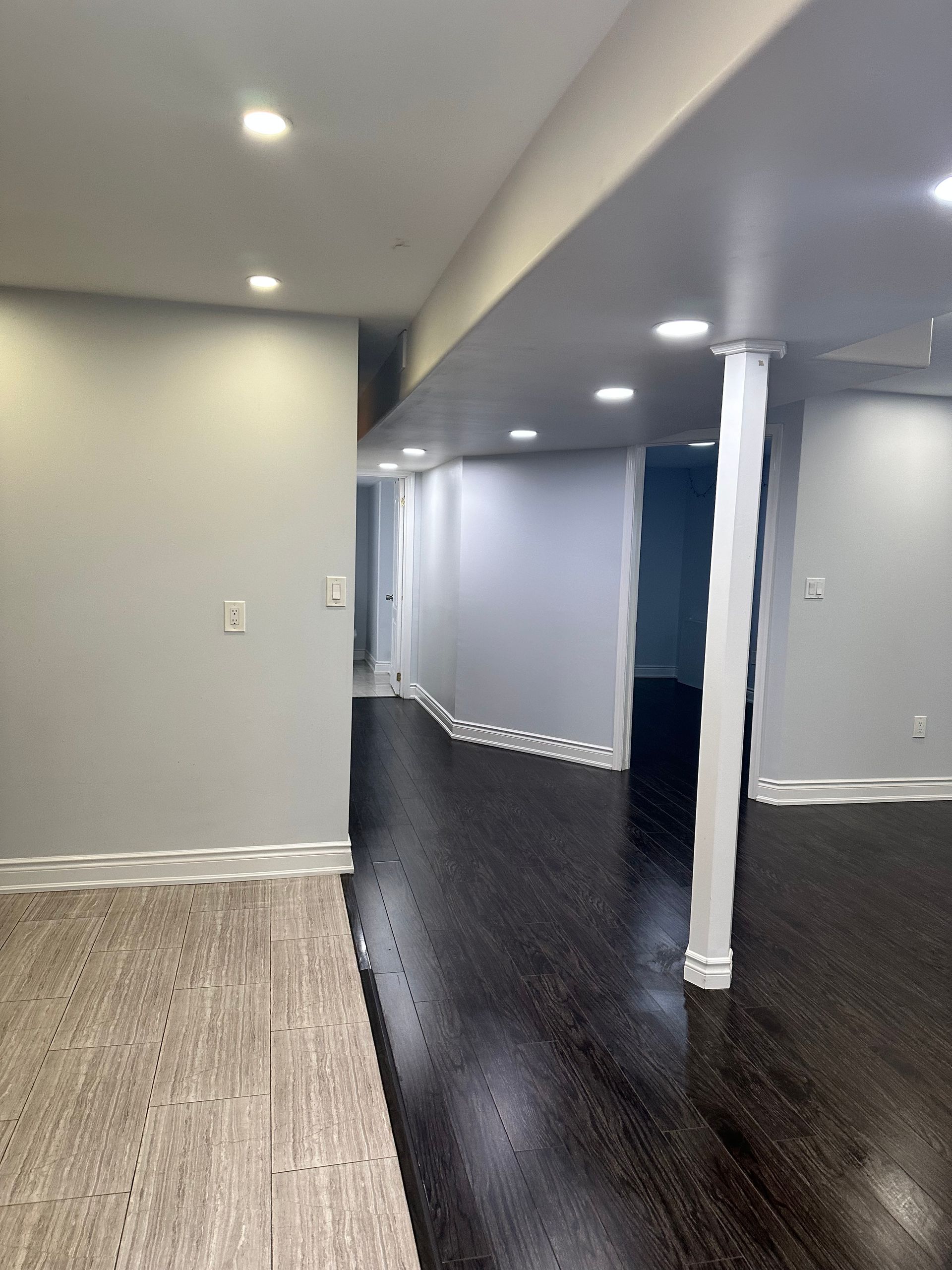 An empty basement with hardwood floors and white walls.