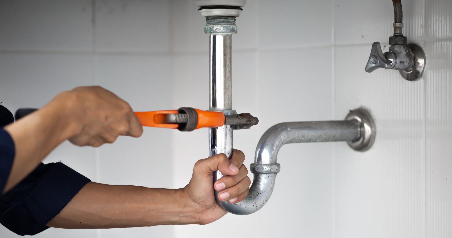 A Man Is Fixing A Pipe With An Orange Wrench — Springville, UT — Blue Plumbing and Drain Cleaning