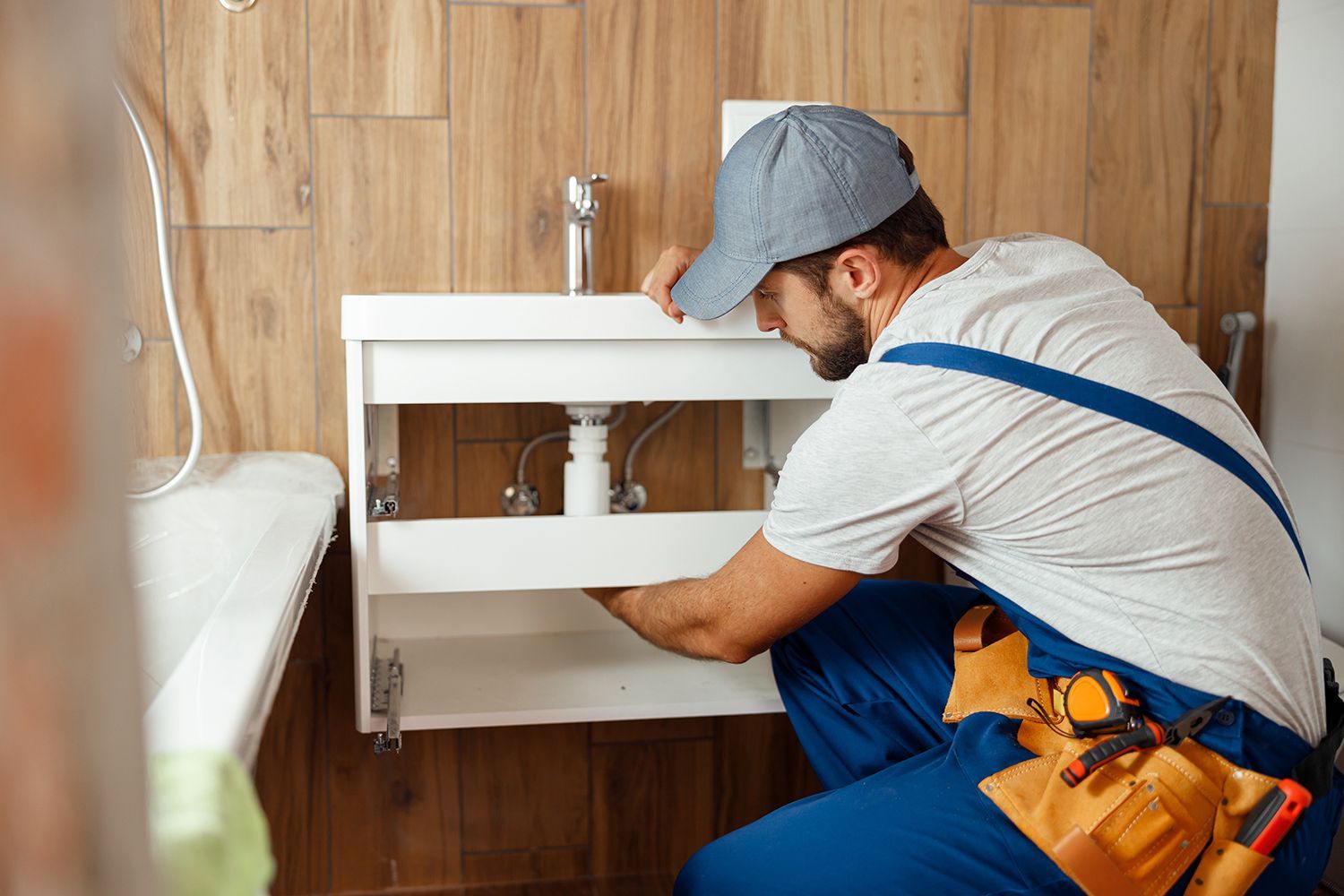 Plumber installing and tightening pipes under a bathroom sink.