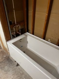 A white bathtub is sitting in a bathroom under construction.