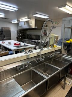 A kitchen with three stainless steel sinks and a faucet.
