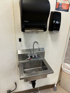A stainless steel sink is sitting on a wall next to a paper towel dispenser.