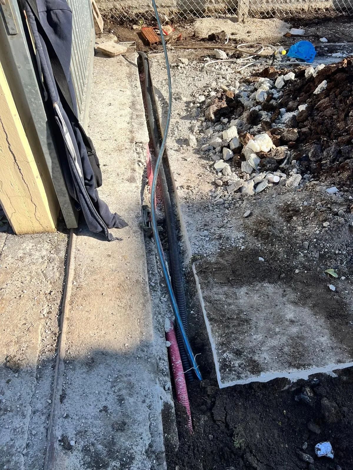 Un tubo blu e un paletto rosa in una trincea che corre lungo una fondazione in cemento in un cantiere all'aperto.