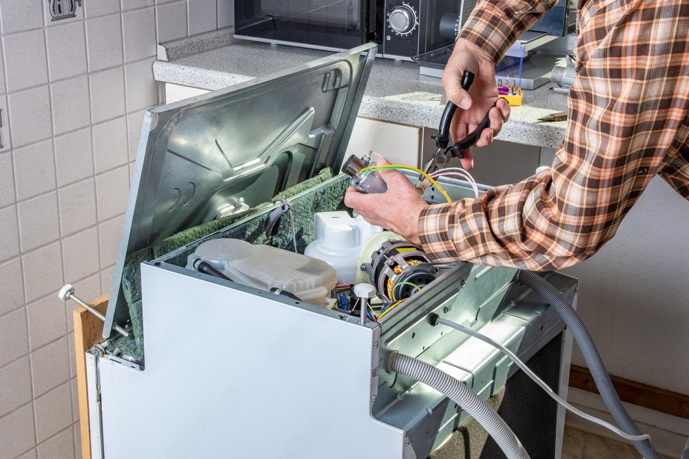 A man is fixing a dishwasher in a kitchen.