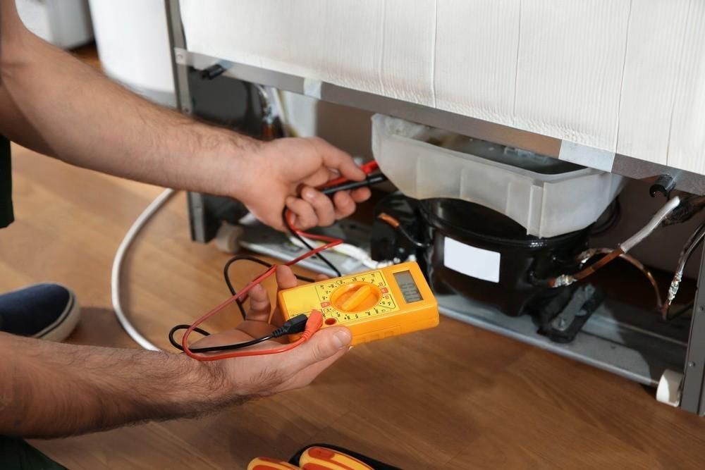 A man is fixing a refrigerator with a multimeter.