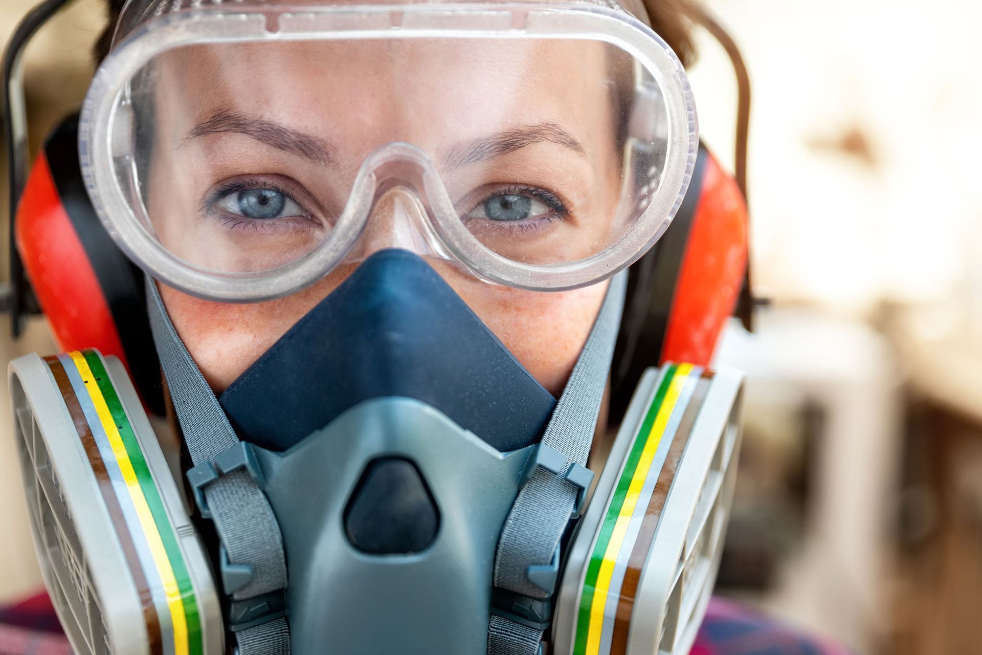 Mujer que usa gafas de seguridad, protección para los oídos y máscara respiratoria, en el interior.