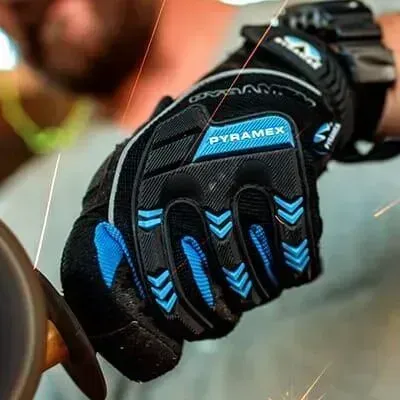 Persona que lleva un guante de trabajo Pyramax negro y azul moliendo metal, mientras saltan chispas.