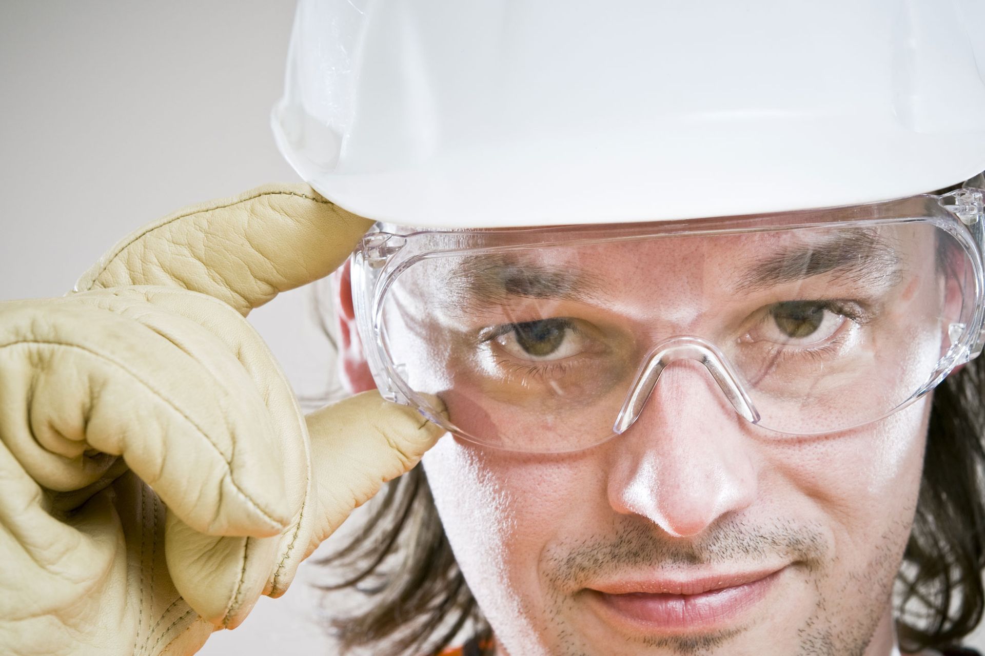 Persona que usa gafas de seguridad, casco y guantes de trabajo, ajustándose las gafas.