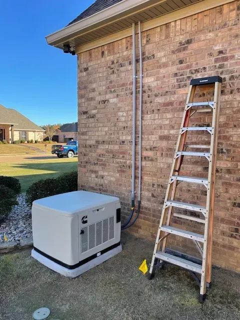 Generator unit next to a brick building with a ladder, pipes, and blue sky in the background.