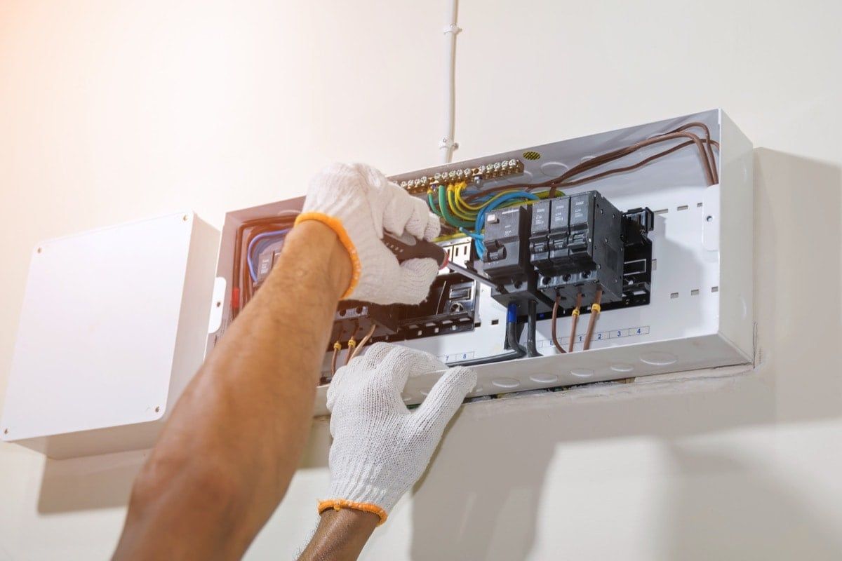 Electrician working on electrical panel, wearing gloves.