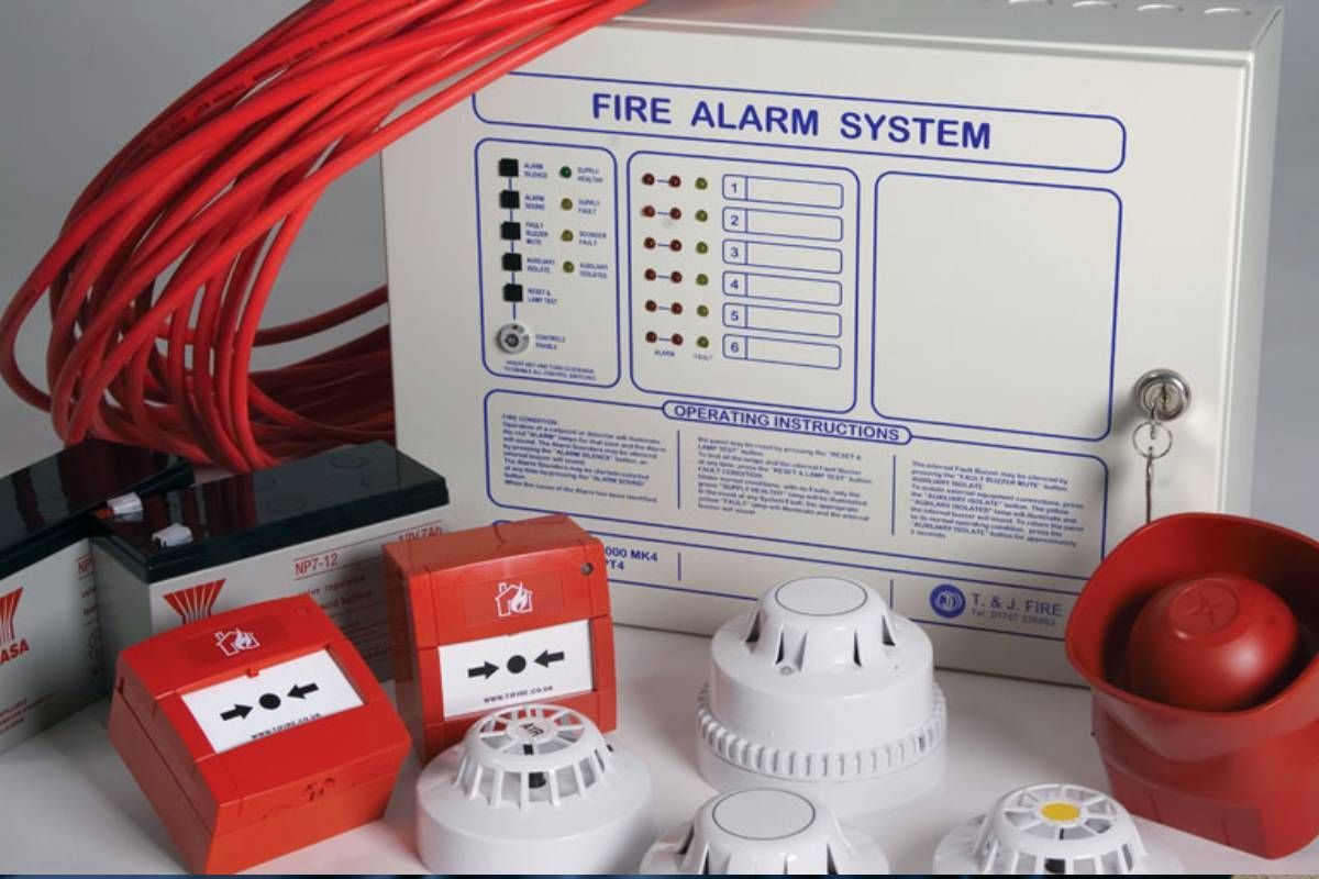 Fire alarm system components: control panel, red wiring, batteries, pull stations, smoke detectors, and a horn.