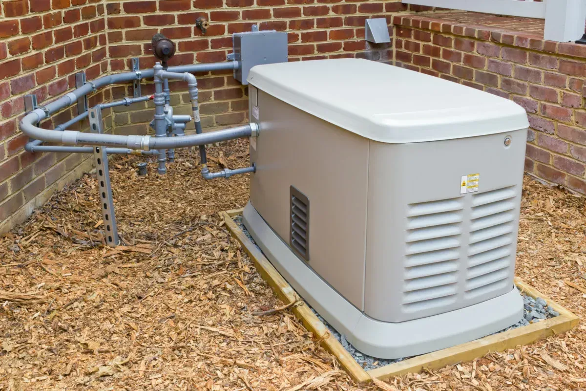 Standby generator outside a brick building, with fuel line and vents.