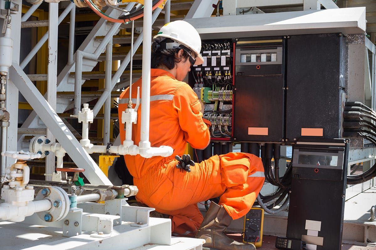 Person in orange jumpsuit working on electrical panel outdoors.