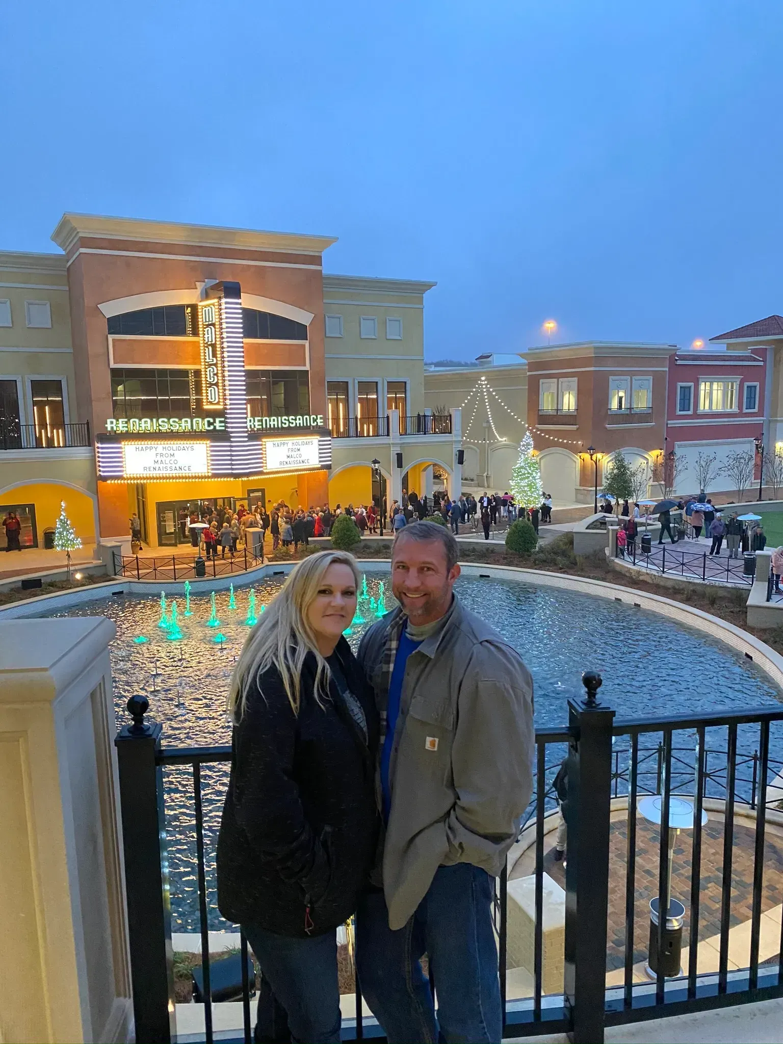 Couple in front of a shopping center with a fountain, Christmas lights, and a theater.