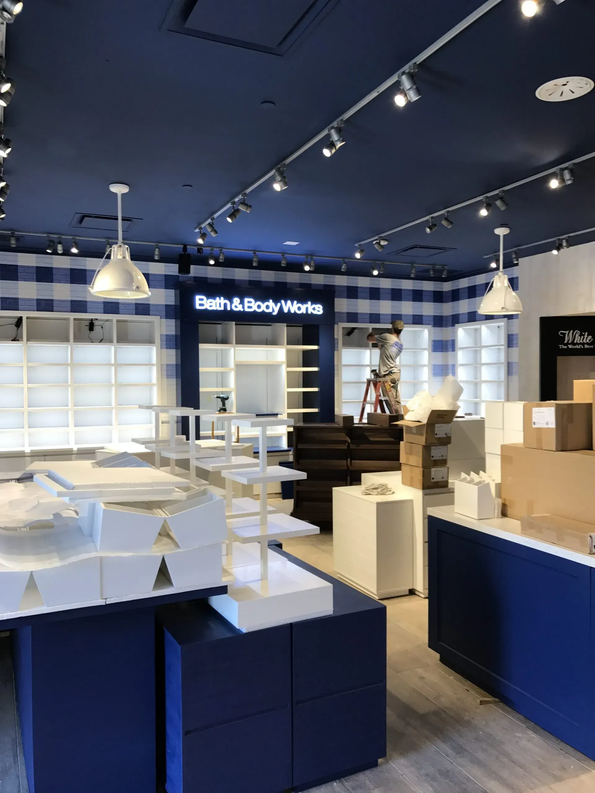 Interior of a Bath & Body Works store under construction, featuring blue and white decor, shelving, and lighting.