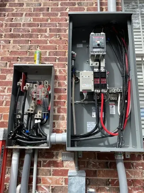 Electrical boxes mounted on a brick wall, containing wires, breakers, and conduits.