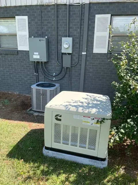 A Cummins generator and AC unit beside a building with gray brick and electrical boxes.