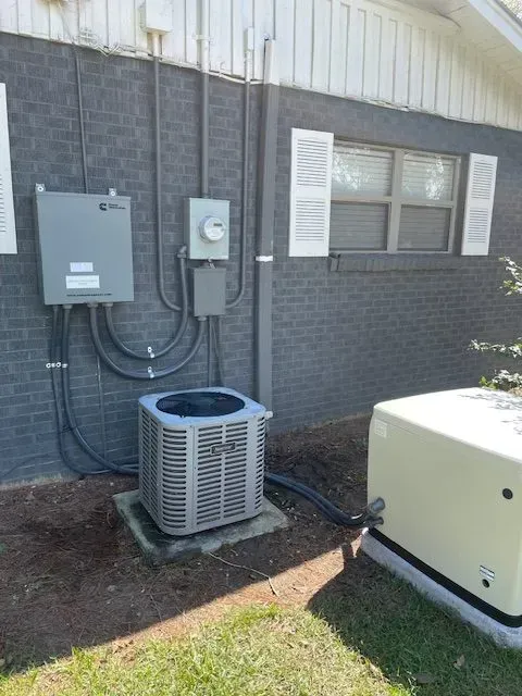Exterior electrical setup: AC unit, generator, power boxes, and conduits on a brick wall.