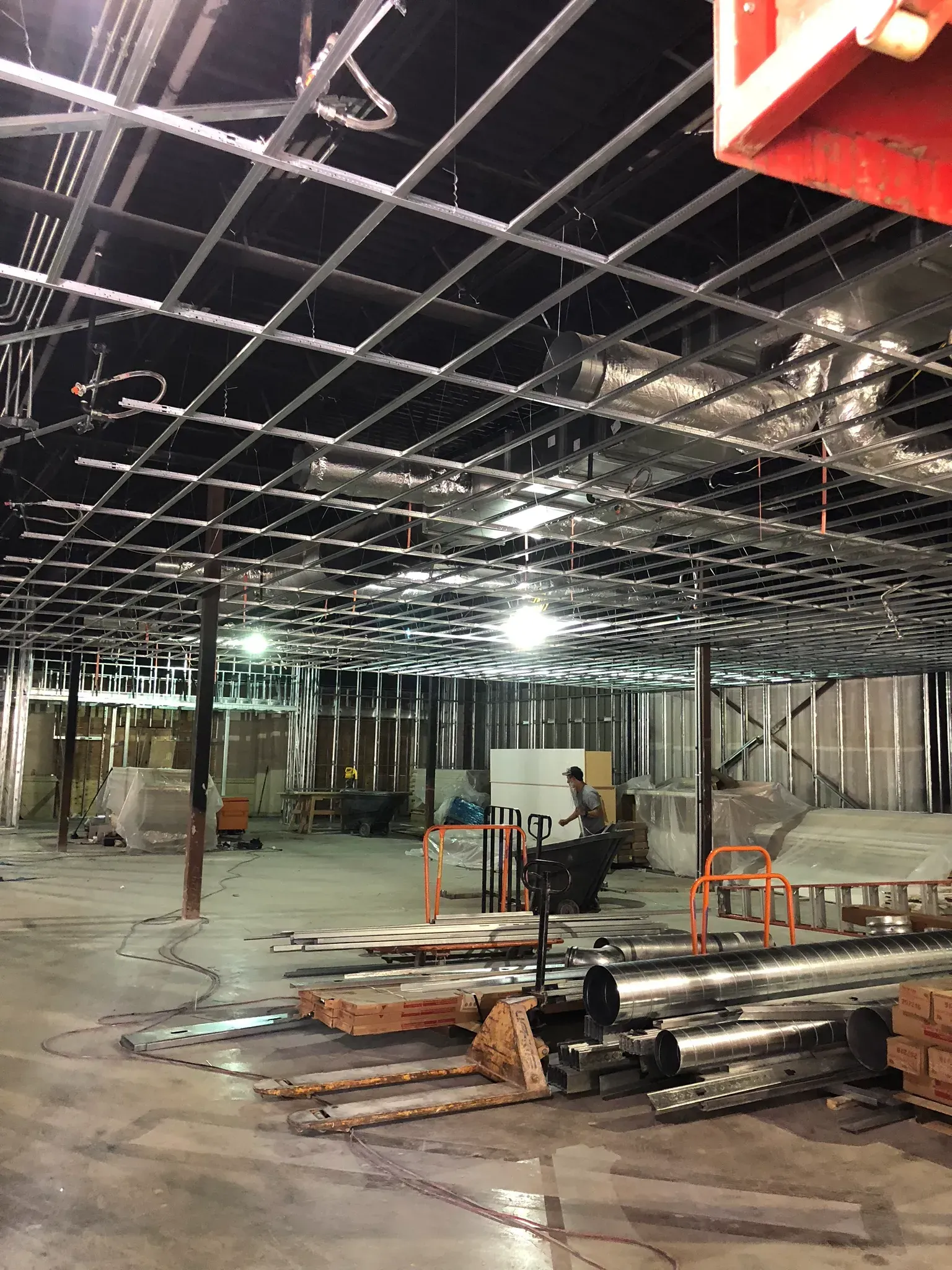 Interior view of a construction site. Metal ceiling grid and exposed walls. Person working in the distance.
