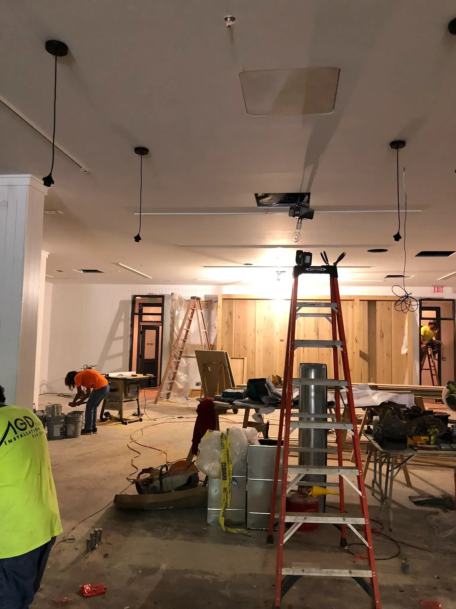 Construction site: Workers inside a room with ladders, tools, and exposed wiring.
