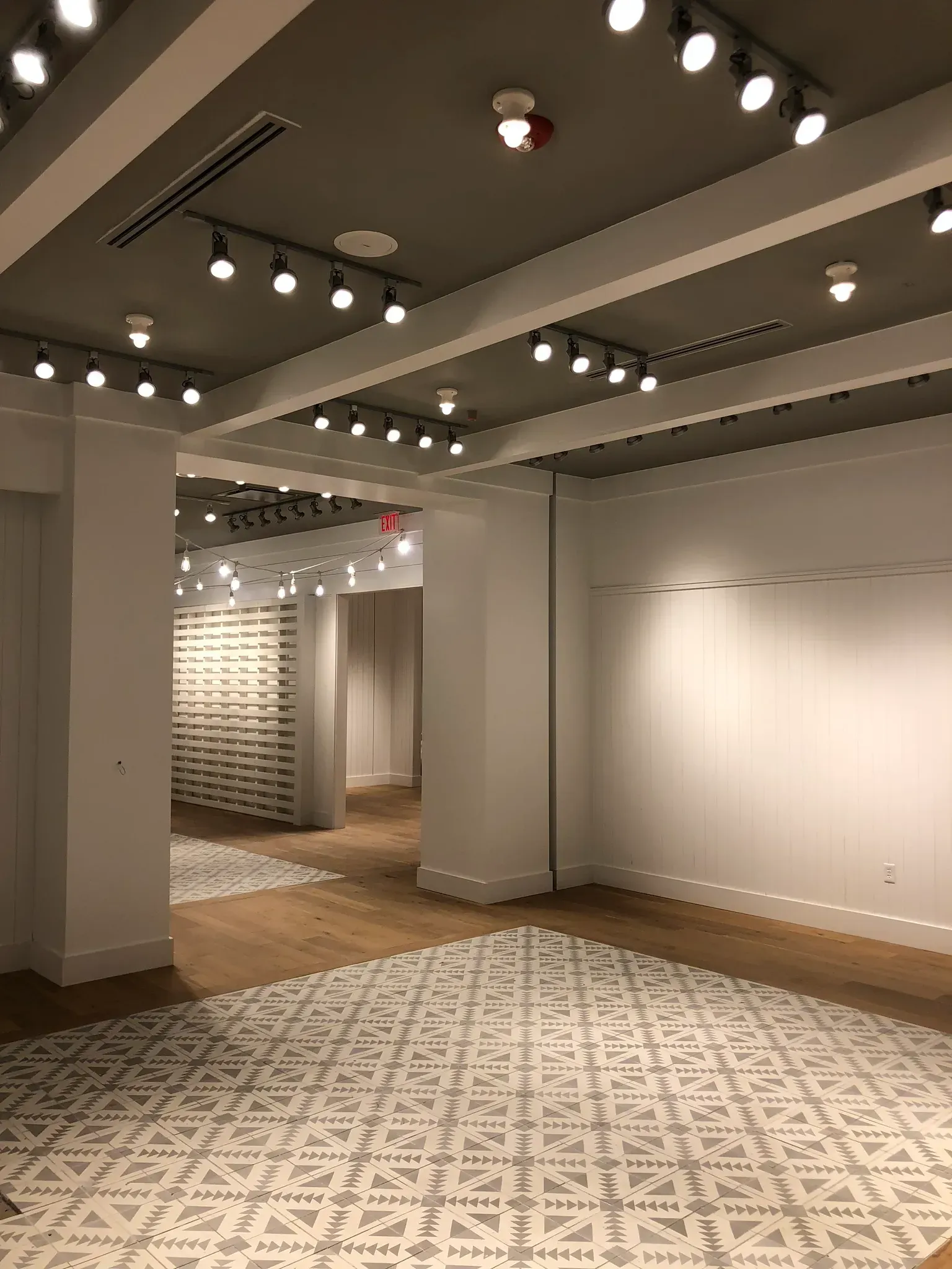 Empty retail space with white walls, track lighting, patterned floor, and wooden floors.