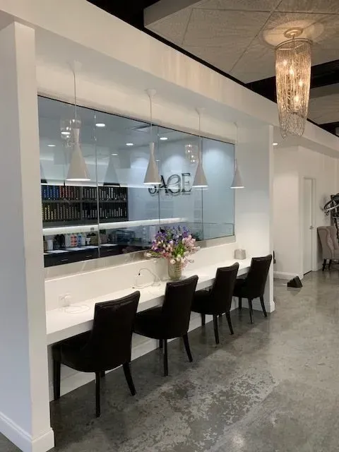 A beauty salon with a row of dark chairs at a white countertop, large window behind it.