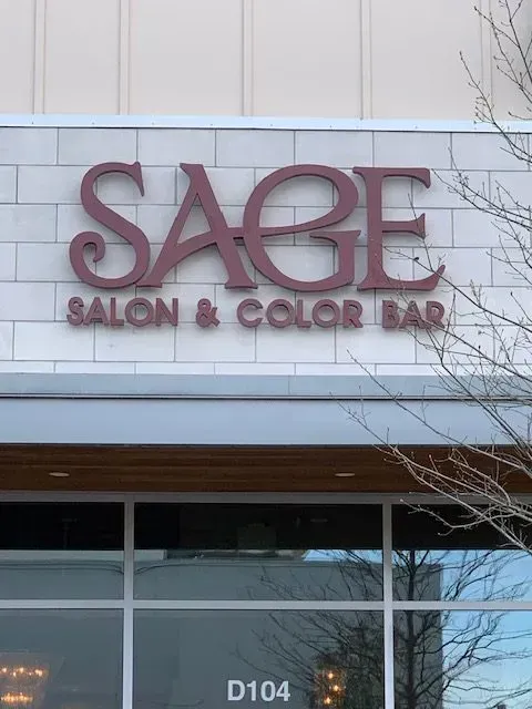 Sign for Sage Salon & Color Bar, mauve lettering on white brick facade, above storefront.